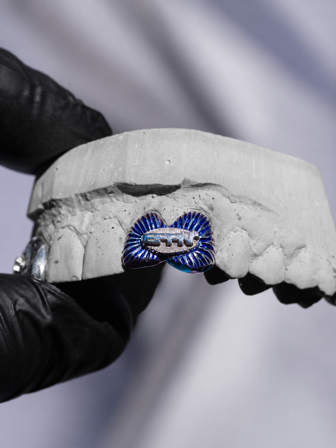 Blue enamel grillz in silver with a hand painted fan detail and engraved logo, shown on dental mould