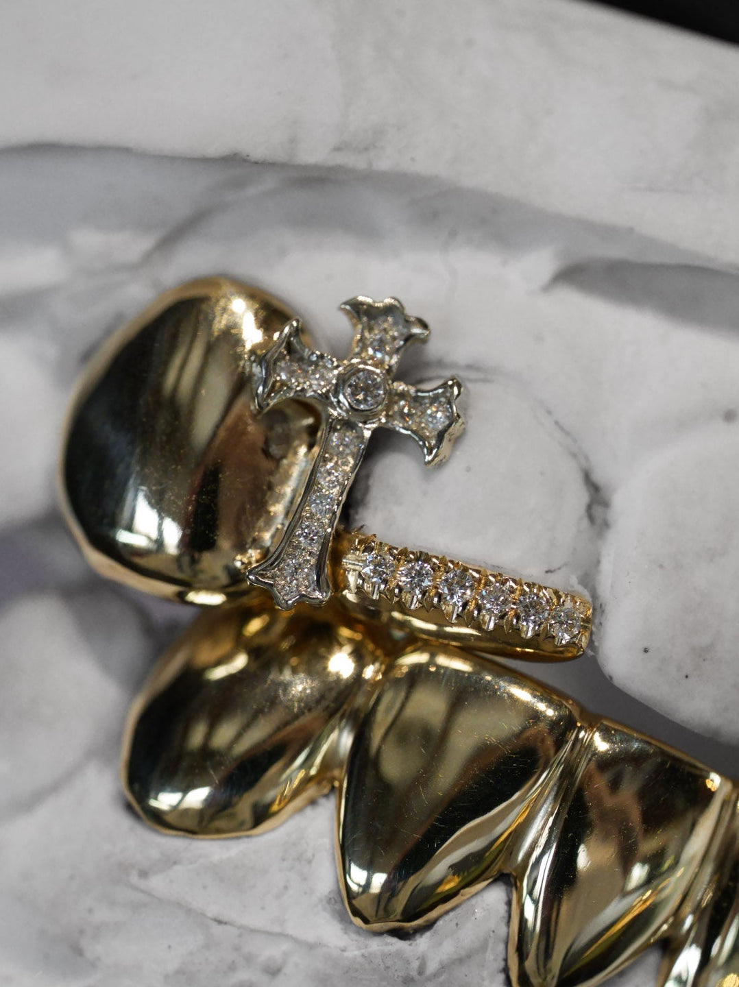 Custom designed grillz in 18k yellow gold with a cross detail and pavé diamond row, shown on dental mould