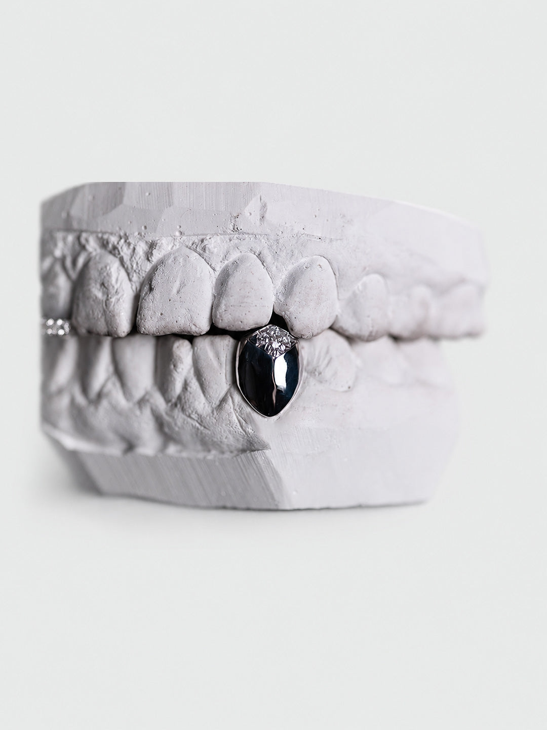 Cluster set diamond tip grillz on a single lower tooth in white gold, shown in a closed bite 