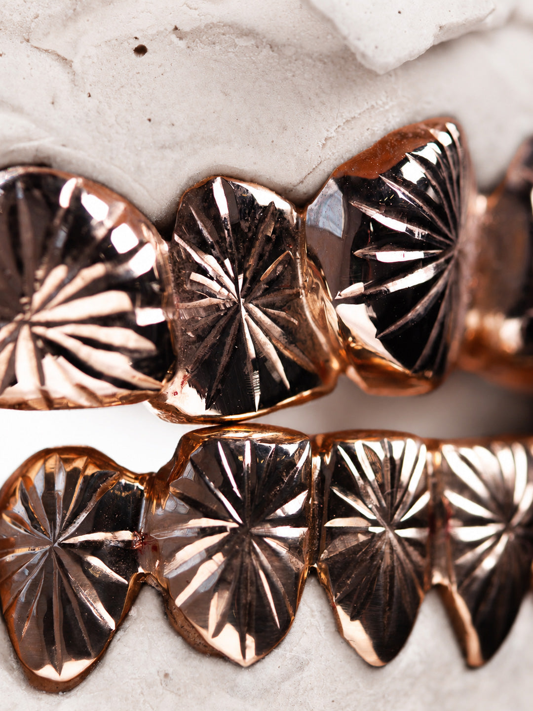 Engraved rose gold grillz with a hand cut sunburst pattern across the top and bottom rows